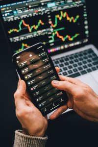 Hands holding smartphone with stock app, laptop displaying charts. Perfect for financial and technology themes.